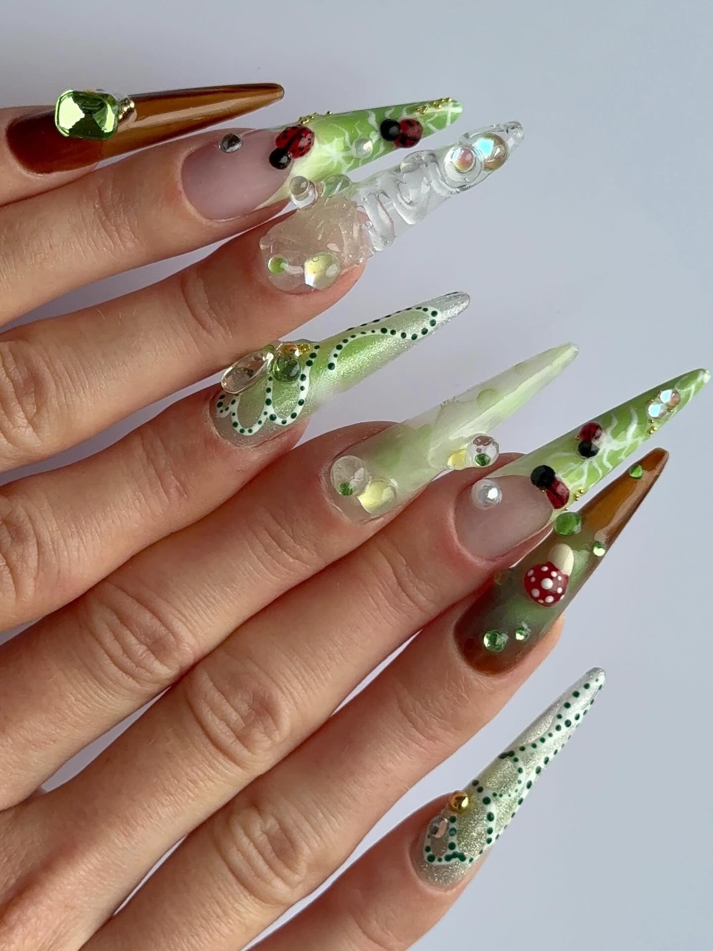 Nail art vert nature en 3D avec coccinelles, champignons et détails sculptés, finition stiletto.
